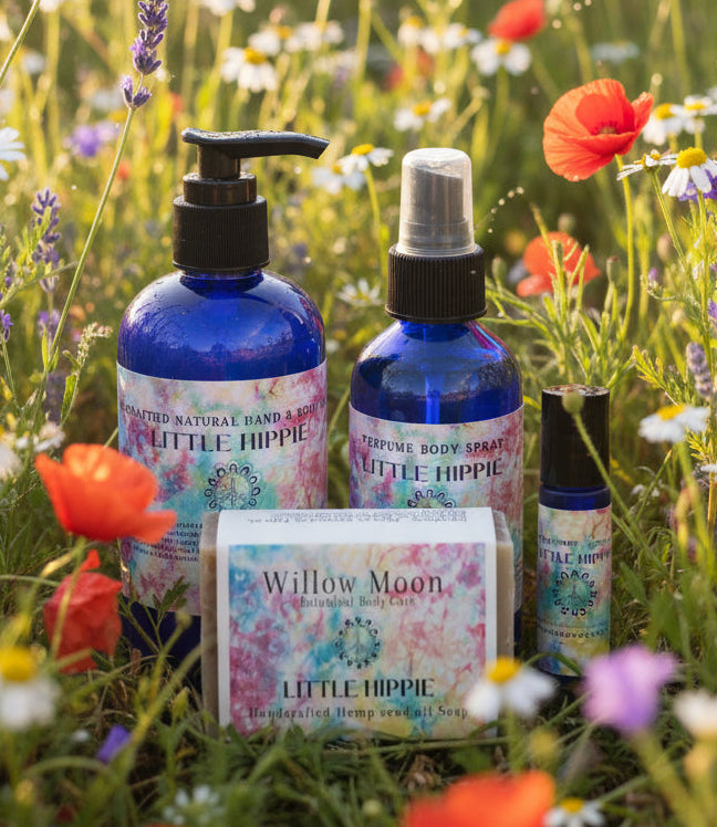 Natural body care products in a field of wildflowers. Picture includes a Little Hippie Body Lotion, body spray, soap and roll on perfume
