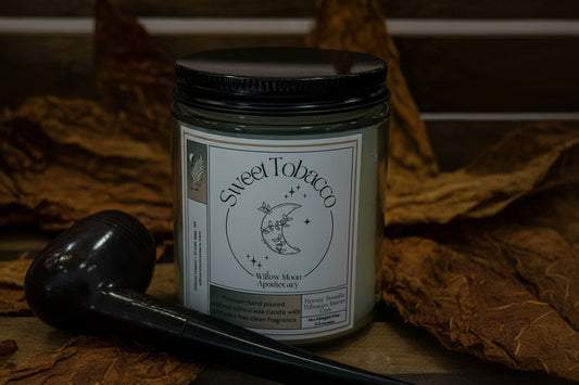 Candle jar labeled 'Sweet Tobacco' by Willow Moon Apothecary on a wooden surface with a pipe.