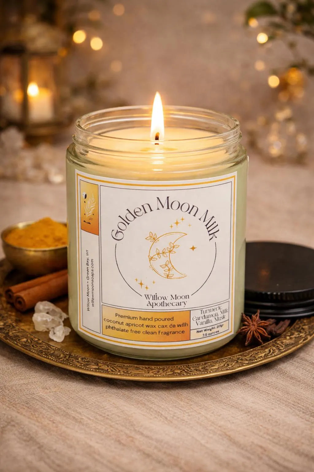 A lit candle in a clear glass jar sits on an ornate gold tray with a warm bokeh background. The label reads 'Golden Moon Milk' by Willow Moon Apothecary.