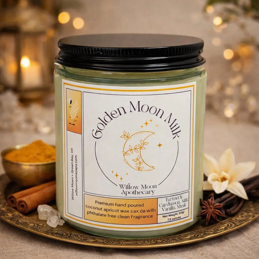A jar candle labeled 'Golden Moon Milk' by Willow Moon Apothecary, set on an ornate tray with cinnamon sticks, a flower, and warm blurred lights in the background.